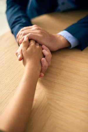 Practicing compassion with professionalism. a businessman and businesswoman compassionately holding hands at a table.の写真素材