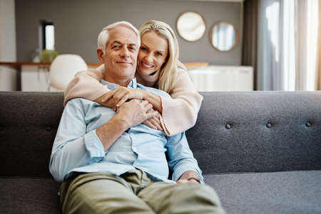 Love each other...a lot. a mature woman hugging her husband on the sofa at home.の写真素材