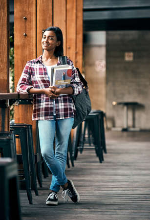 Enjoying being a student. a young female student holding textbooks outside on campus.の写真素材