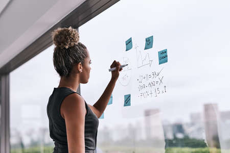 Theres a new plan on the wall. a young businesswoman writing on a glass wall in an office.の写真素材