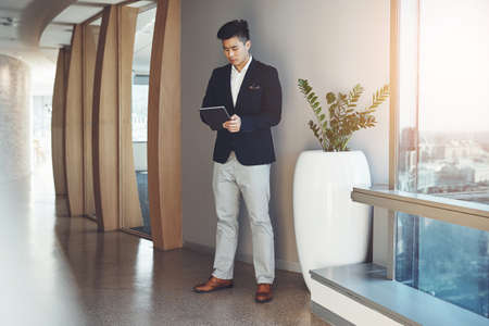 Staying connected and updated with his business demands. a young businessman using a digital tablet in an office.の写真素材