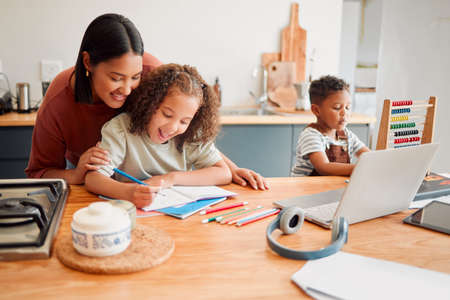 Mother and children doing homework at kitchen table, bonding and enjoying family time at home. Affectionate parent helping daughter draw or sketch after online education program for distance learningの写真素材
