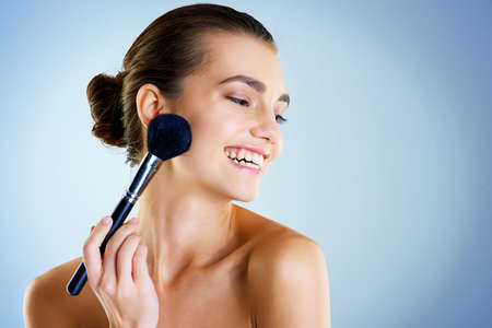 Highlighting her gorgeous features. Studio shot of a beautiful young woman applying makeup with a...