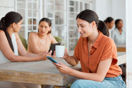 Businesswoman, designer or worker on her phone texting, reading and replying to sms with smile while drinking coffee at work. Professional female relaxing, searching and browsing during her lunch.の写真素材