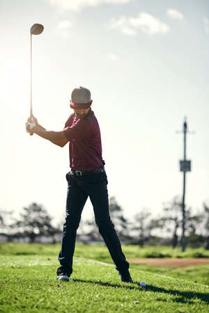 Pull back and swing. a focused young male golfer about to swing and play a shot with his golf club outside on a course.の写真素材