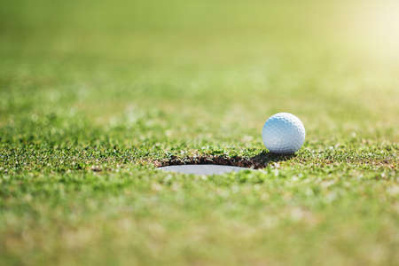 So close yet no cigar. Closeup shot of a golf ball on the edge of a hole outside on a golf course during the day.の写真素材