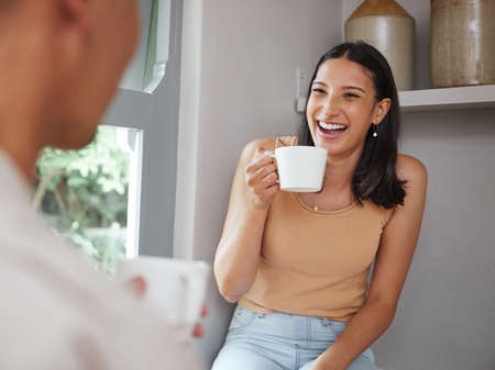 Happy, carefree and laughing woman drinking coffee in the morning and having fun with her boyfriend at home. Young and excited female laughs at a funny joke while and enjoying time with her partnerの写真素材