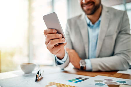 Never far from all his connections. Closeup shot of an unrecognizable businessman using a cellphone in an office.の写真素材