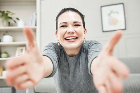 Happy, smiling and laughing woman reaching out her arms for a hug, embrace or holding while relaxing alone at home. Portrait of a relaxed, content and cheerful female giving embrace and being playfulの写真素材