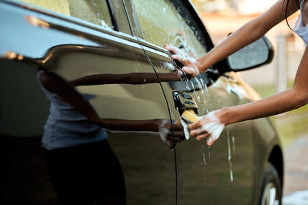 Paying attention to detail. an unrecognizable young child washing their parents car outside during the day.の写真素材