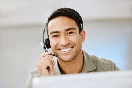 Smiling, friendly call center agent with headset for online consulting in an IT tech agency. Face of male ecommerce support professional offering virtual assistance to web user or contact us hotlineの写真素材
