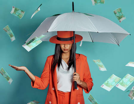 Money, fashion and rich lady being showered by cash while holding umbrella for insurance, protection and cover showing her wealth after payout. Winning luxury woman with dollar bills in the airの写真素材