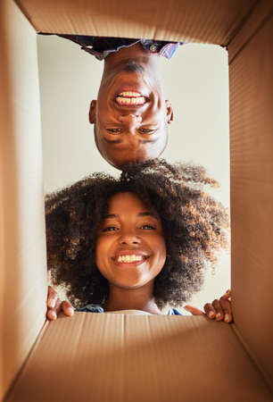 Whats in the box. Low angle portrait of a cheerful couple looking into a cardboard box at home...