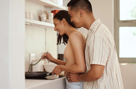 Romantic, loving and caring couple cooking and bonding while hugging in the morning at home. Smiling...