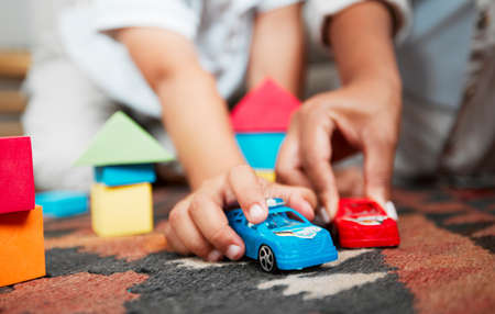 Closeup hands playing with fun toys, cars and building blocks in a home living room. Parent bonding, having fun and enjoying family time with a playful, small and little child during childhood funの写真素材