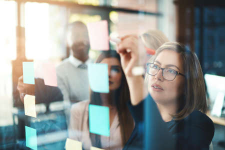 Marketing leader planning and writing on sticky notes on wall while support and sharing vision or...