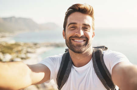 Smiling at the summit. Cropped portrait of a handsome young man taking selfies while hiking in the mountains.の写真素材
