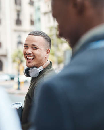Real life young man portrait in the street with headphones, enjoying music on a playlist app looking happy, stressless and cool. Normal face of a millennial with wireless tech outside an urban cityの写真素材