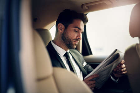 Reading newspaper early in the morning. a confident young businessman reading the newspaper while...