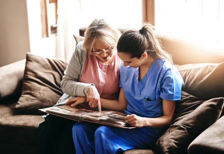 Triggering some old memories. a nurse and a senior woman looking at a photo album together.