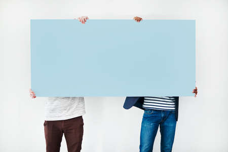 For your attention... Studio shot of two men covering themselves with a blank placard against a white background.の写真素材