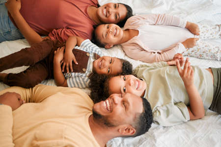 Happy mother, father and children together as a family lying, relaxing and bonding in the bedroom at home. Mom, dad and kids smiling, free and loving quality time together. Siblings with parentsの写真素材