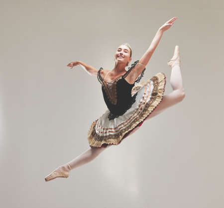 Elegant ballet dancer dancing with a vintage style, jumping and performing in a studio. Portrait of a skilled, talented and young ballerina leaping high in the air enjoying her performanceの写真素材