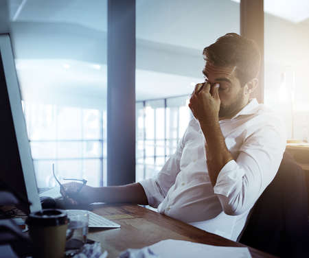 He cant take much more of this. a young businessman looking stressed while working late in the...