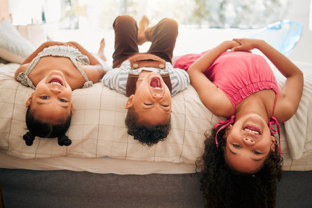 Silly kids playing upside down on bed enjoy and having fun together in parents bedroom. Happy children or siblings bonding and enjoying childhood together at cozy, warm and comfortable family homeの写真素材