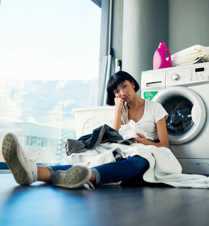 I miss my mom for this. an attractive young woman looking bored while doing the laundry at home.の写真素材