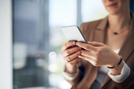 Connected to her vast business network. Closeup shot of an unrecognizable businesswoman using her cellphone in an office.の写真素材