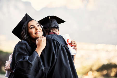 We did it. two students hugging each other on graduation day.の写真素材