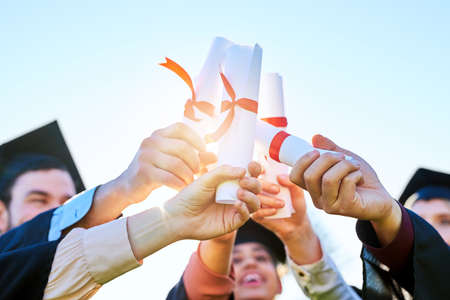 Well pursue greatness with these. a group of students holding their diplomas together on graduation day.の写真素材