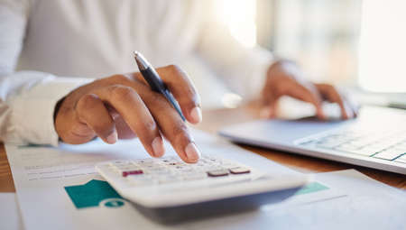 Finance, accounting and fintech, a man on a computer and calculator working out his business budget strategy. Businessman at his office desk, laptop, money management and financial investment online.の写真素材