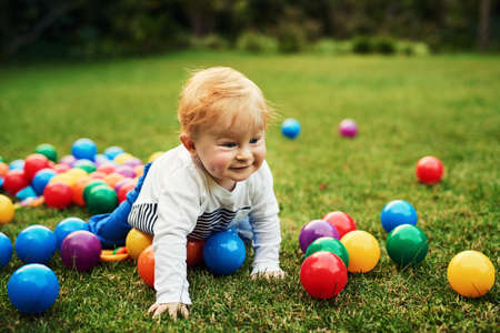 Colourful balls here I come. an adorable little boy playing in the backyard.の写真素材
