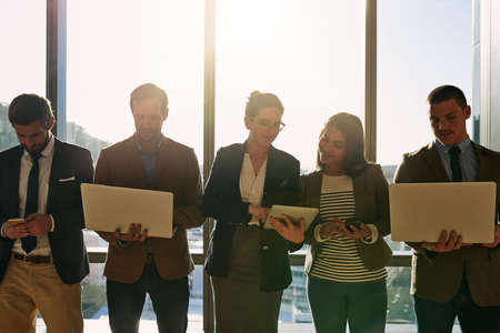 Wireless is the only way to work. a group of businesspeople using wireless devices while standing in the office.の写真素材
