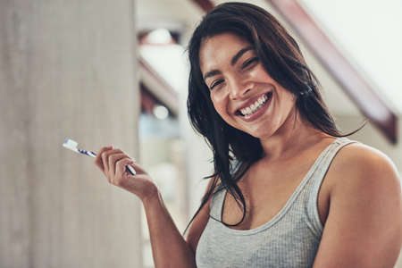 Time to shine these pearls. Portrait of an attractive young woman brushing her teeth at home.の写真素材