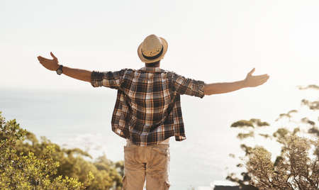 This is what it means to be free. Rearview shot of an unrecognizable young man standing with his arms outstretched while hiking in the mountains.の写真素材