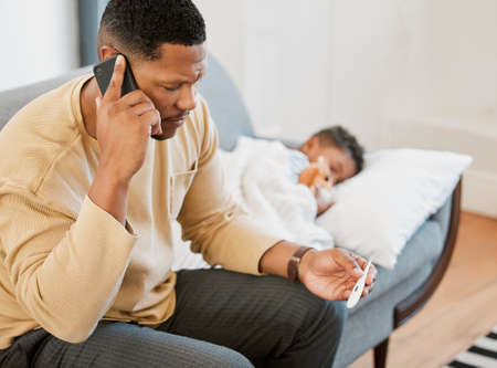 Worried father concerned, caring for sick son calling a doctor and taking temperature check of his...