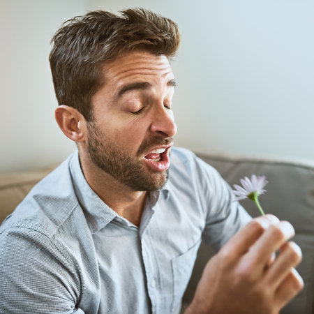 Flowers make me sneeze. a carefree young man about to sneeze while holding a flower in his hands and...