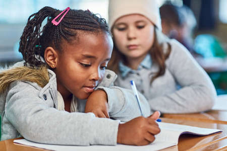 Learning from each other. elementary school girls doing school work together in the classroom.の写真素材