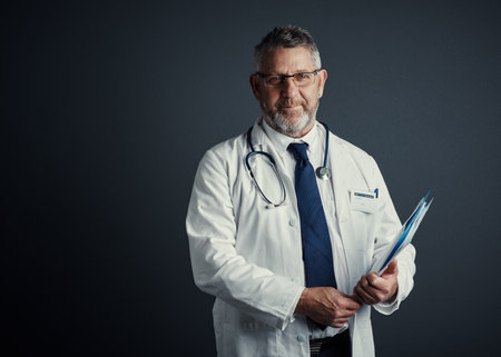 These medical records tell me everything. Studio portrait of a handsome mature male doctor holding...