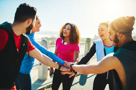 Who will be first today. a group of young cheerful friends forming a huddle before a fitness exercise outside during the day.の写真素材