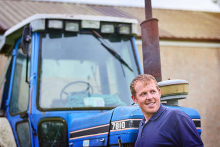 He believes in the farming dream. a farmer standing next to a tractor on a farm.の写真素材
