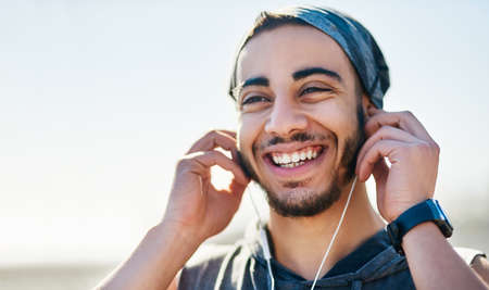 Deciding on the tunes to keep him moving. a sporty young man listening to music while exercising outdoors.の写真素材