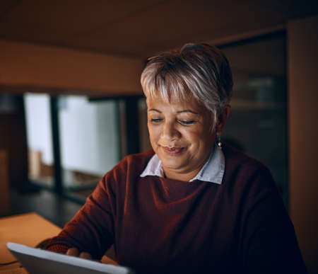 Night time business browsing. a mature businesswoman using a digital tablet while working late in an...