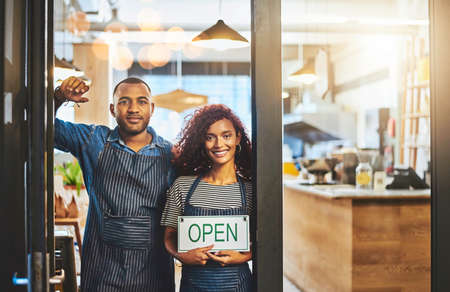We are open for business. Portrait of two young entrepreneurs holding an open sign in their store.