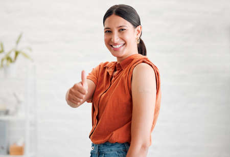 Positive young woman treated with covid vaccine injection, gestures thumbs up and showing her arm to...