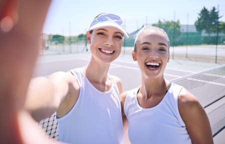 Selfie taking team of female tennis players on the court after a game, match or tournament portrait. Fit sporty teammates, athletes or professionals relax after being active, exercise and trainingの写真素材