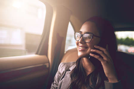 Ill be in the office shortly. a young businesswoman talking on a cellphone in the backseat of a car.の写真素材